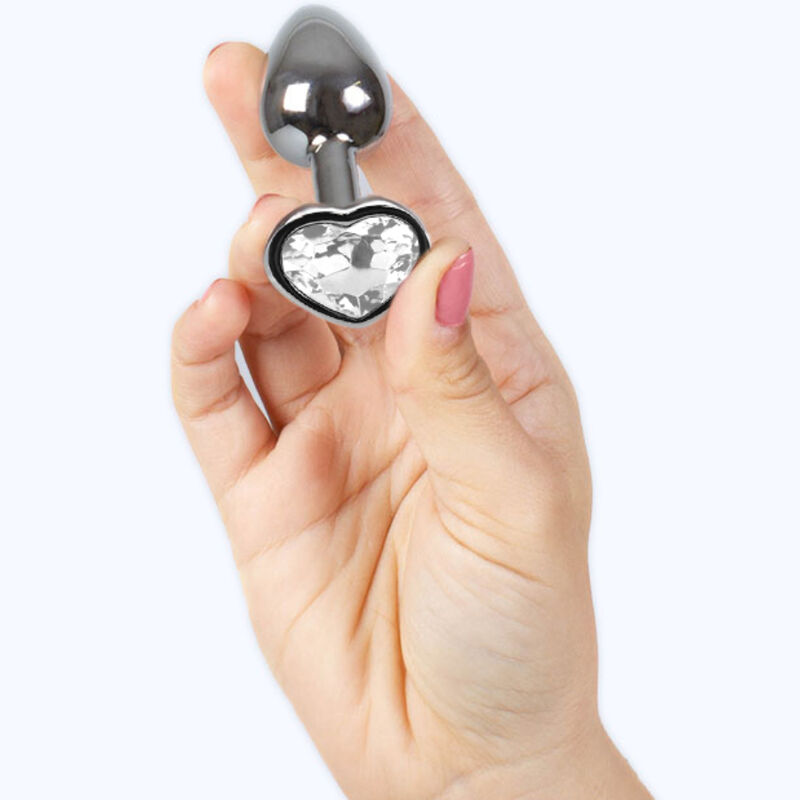 Detalle del tapón anal metálico Secretplay Toys con base en forma de corazón transparente, sostenido en la mano.