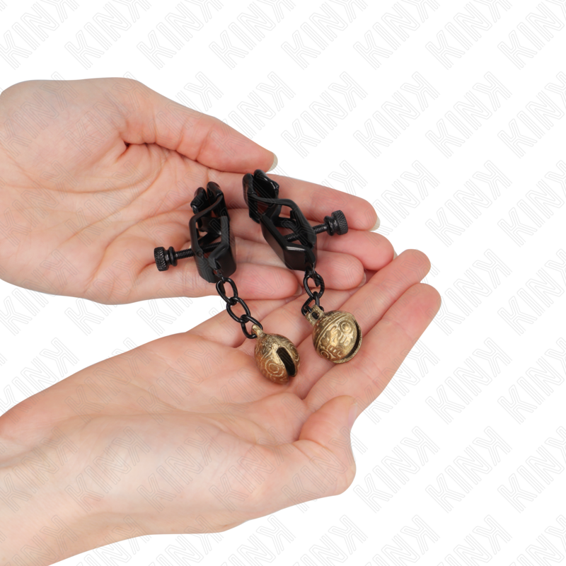 Detalle de KINK NIPPLE GRIP: pinzas negras para pezones con campanillas, sujetas en las manos.