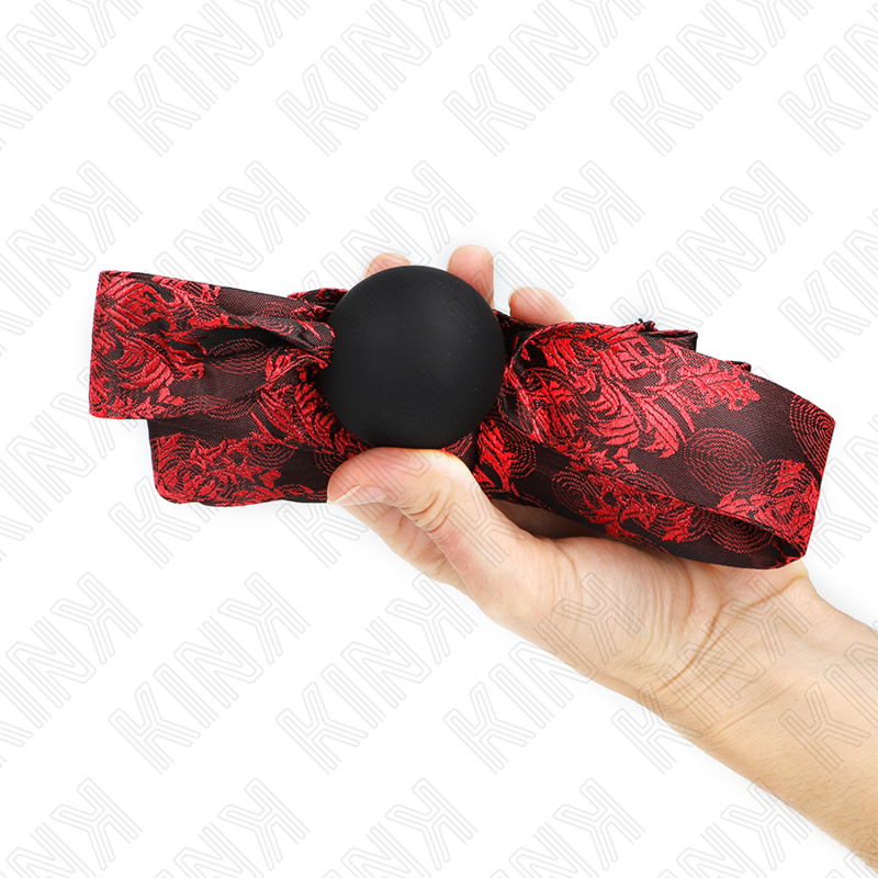 Mordaza de bola de silicona KINK Scandal Model 2, con correa roja estampada, en la mano.