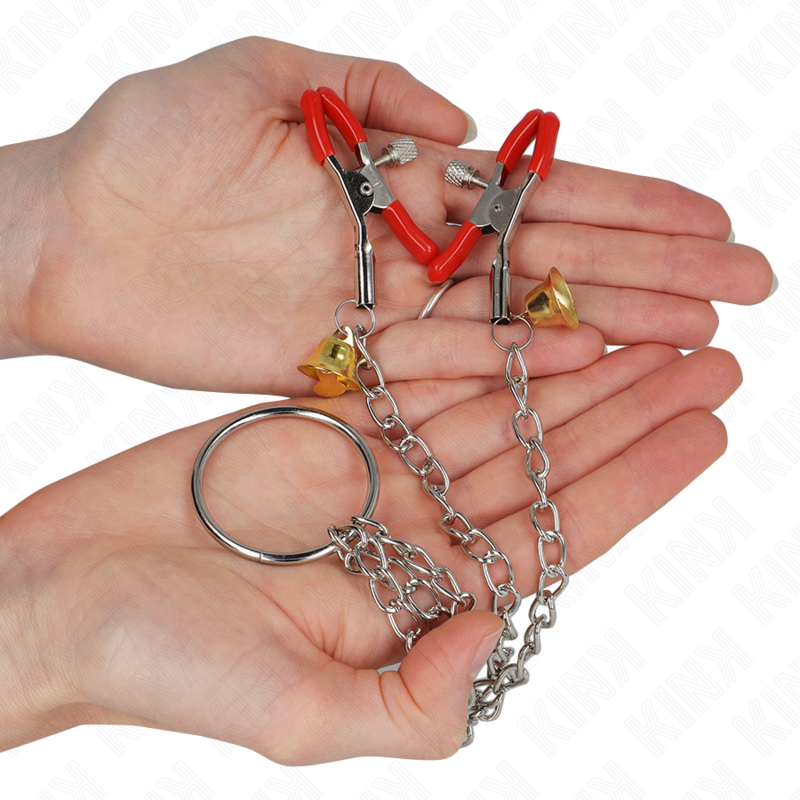 KINK NIPPLE GRIP en rojo con tres pinzas, campana dorada y cadena metálica, sujetado con las manos.